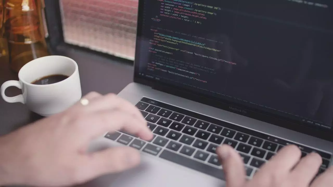 A developer writes code on a laptop next to a cup of coffee